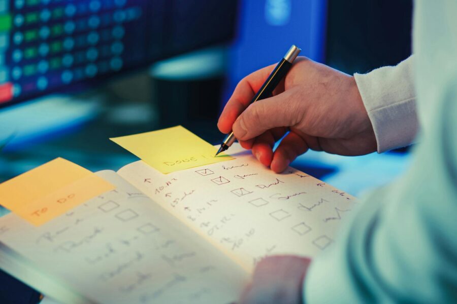 Person writing weekly priorities notebook desk