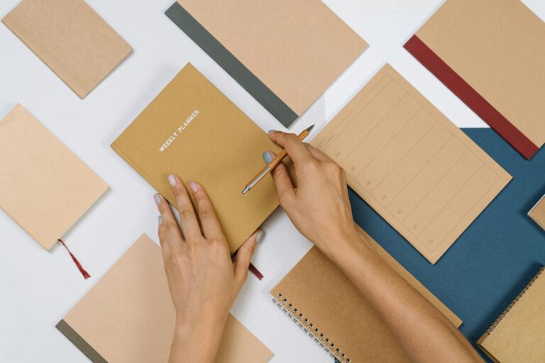 Person writing weekly priorities notebook desk